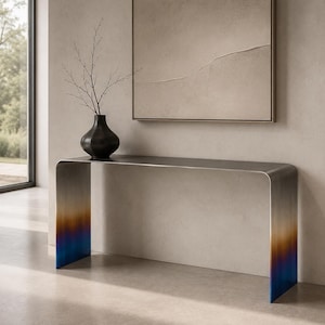 Könnte beinhalten: Ein Konsolentisch aus Metall mit glattem, geschwungenem Design und einem Farbverlauf, der von einer metallisch silbernen Oberseite zu einer Basis in Orange, Violett und Blau übergeht. Eine dunkle, mattierte Vase mit dünnen Zweigen steht darauf.