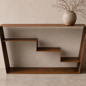 Op de afbeelding: Een bruine metalen consoletafel met een trapeziumvormig frame en een getrapt interieurontwerp met planken. De tafel heeft een glad, solide oppervlak en is bekroond met een ronde, textuurrijke beige keramische vaas met dunne takjes.