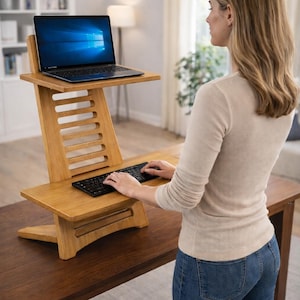 May include: A wooden DIY standing desk with a laptop and keyboard. The desk has a tiered design with a top shelf for the laptop and a lower shelf for the keyboard. The text "DIY PLAN" is in a red rectangle at the top.