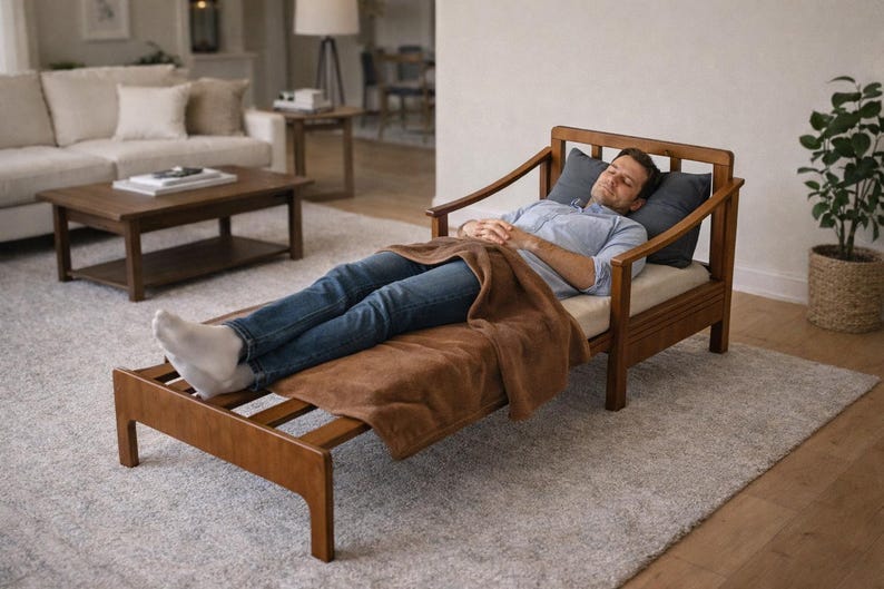 May include: Wooden chaise lounge with a brown blanket. The lounge has a light-colored cushion and two gray pillows. The frame is made of wood. The lounge is in a living room with a rug and a sofa.