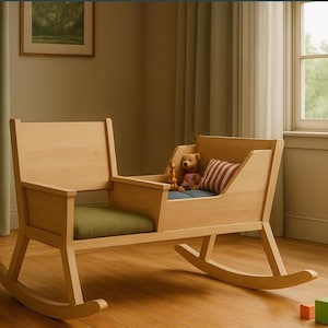 May include: A light-colored wooden rocking cradle with a green cushion and a small striped pillow. A teddy bear sits inside the cradle. The cradle is on a hardwood floor. A lamp and a window are in the background.