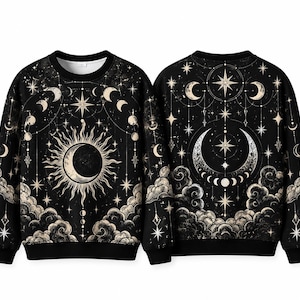 May include: A black long-sleeve sweatshirt featuring a celestial print with a central sun and crescent moon, surrounded by stars, moon phases, and clouds. The design is repeated on the front and back, with a crew neckline and ribbed cuffs.