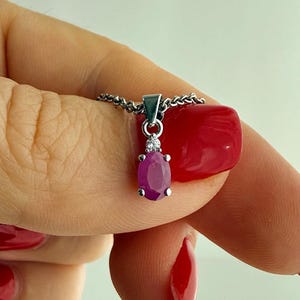 Op de afbeelding: Een zilveren ketting met een ovaal geslepen roze-rode edelsteen hanger. De hanger is aan de bovenzijde voorzien van een kleine heldere steen en hangt aan een fijne zilveren ketting, met een gepolijste metalen afwerking.