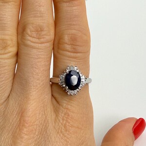 Natural blue sapphire engagement ring held between two fingers, alternating baguette and round white stones forming a structured halo
