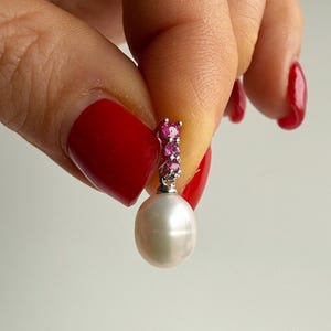 May include: A single pearl earring with a silver-colored top adorned with small pink gemstones. The earring features a large, lustrous white pearl. The design is elegant and suitable for formal occasions.