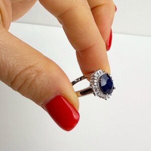 Princess Diana inspired sapphire ring on the ring finger, hand relaxed and oval stone centered in frame against white background