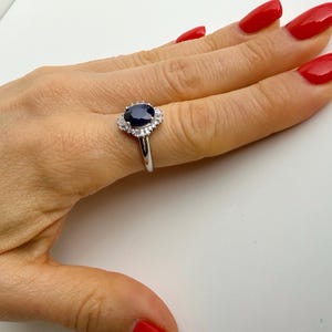 Princess Diana style sapphire ring worn on the ring finger, deep royal blue oval stone contrasting against polished rhodium-plated silver