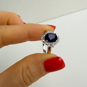 Side profile of a sapphire halo ring held between fingers, showing the elevation of the center stone above the band