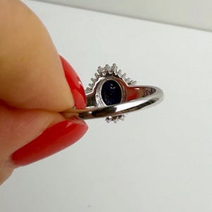 Sterling silver band with sapphire ballerina halo seen from the back of the hand, showing ring scale against the finger