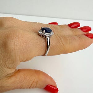 Silver ring with deep blue sapphire and mixed-cut white stone halo seen from a low angle, emphasizing layered setting depth