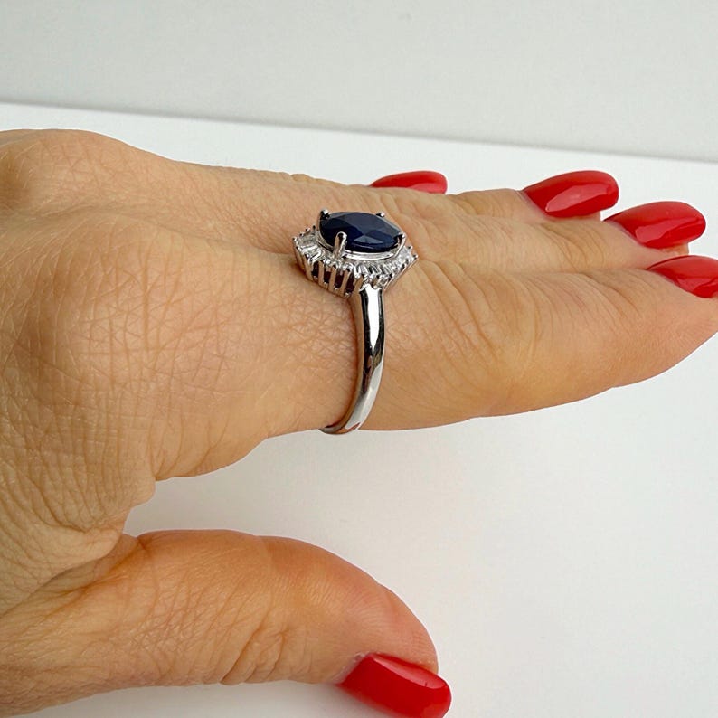 Silver ring with deep blue sapphire and mixed-cut white stone halo seen from a low angle, emphasizing layered setting depth