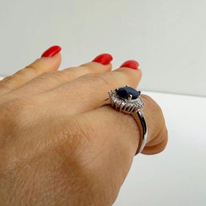 Natural blue sapphire ring in ballerina halo setting held from above, the oval stone deeply saturated against bright surrounding stones