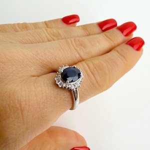 Sterling silver blue sapphire ring centered in a symmetrical baguette and round stone halo, seen straight on from the front