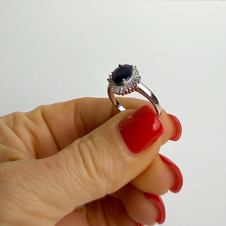 Overhead view of a blue sapphire engagement ring on the hand, symmetrical halo framing the dark center stone evenly