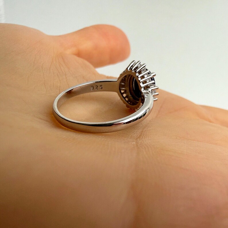 Oval blue sapphire centered in a bright white stone halo, baguette cut detail and open prong construction visible up close​​​​​​​​​​​​​​​​
