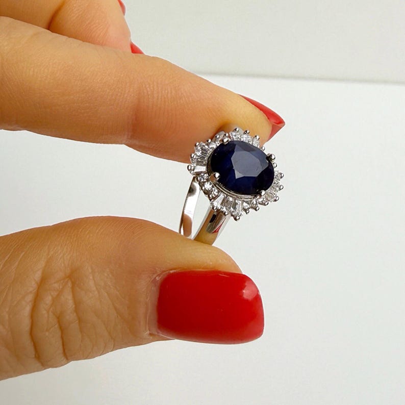 Ballerina halo sapphire ring worn on the finger, baguette stones visible along the lower arc of the halo in sharp detail