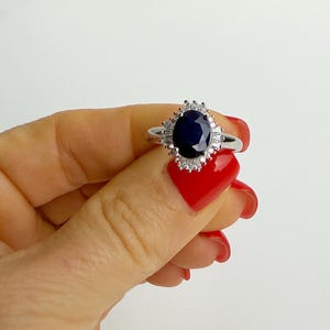 Oval sapphire halo ring viewed from above on a finger, the september birthstone rich and dark against bright surrounding stones