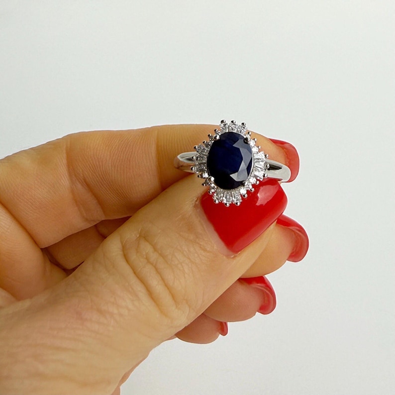 Oval sapphire halo ring viewed from above on a finger, the september birthstone rich and dark against bright surrounding stones
