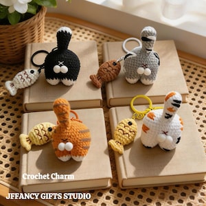 May include: Crocheted cat butt keychains in black, gray, orange, and white, each with a fish charm. The keychains are displayed on books. The text "Crochet Charm" and "JEFFANCY GIFTS STUDIO" are visible.