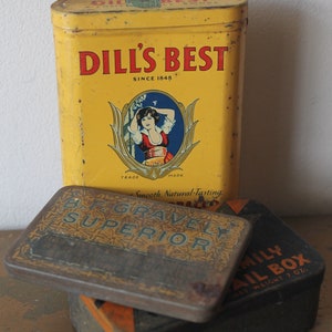 May include: Three vintage tobacco tins. The top tin is yellow with the text "Dill's Best Since 1848" and a picture of a woman in a yellow dress. The middle tin is brown with the text "B.F. Gravelly Superior" in gold lettering. The bottom tin is black with the text "Family Mail Box Net Weight 7 oz."