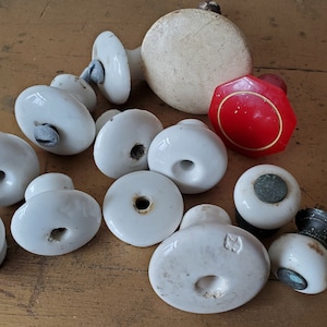 May include: A collection of white ceramic door knobs with a red octagonal knob with a gold trim. The knobs have a variety of styles and sizes.