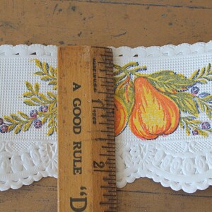 Puede incluir: Borde de encaje blanco con un borde festoneado y un dise&ntilde;o impreso de peras amarillas y naranjas con hojas verdes y bayas moradas. El borde se mide con una regla que dice "A Good Rule" y tiene 5 cm de largo.