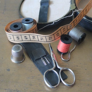 May include: A close-up of a sewing kit containing a thimble, scissors, spools of thread and a tape measure. The tape measure is marked with numbers from 67 to 74.