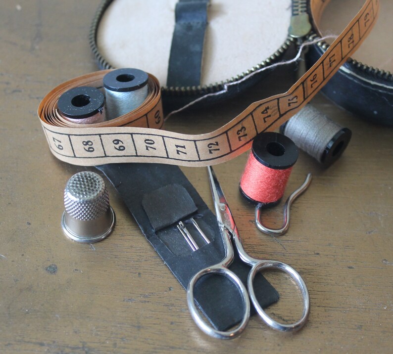 May include: A close-up of a sewing kit containing a thimble, scissors, spools of thread and a tape measure. The tape measure is marked with numbers from 67 to 74.