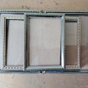 May include: Three silver picture frames with ornate borders, nested inside each other. The frames are empty and ready for photos.