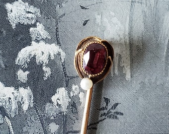 May include: A gold-toned stick pin with a red gemstone set in a gold-toned bezel. The pin has a pearl accent at the top.