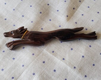 May include: A dark brown wooden carving of a running dog with a gold collar. The carving is detailed and realistic, with a textured surface.
