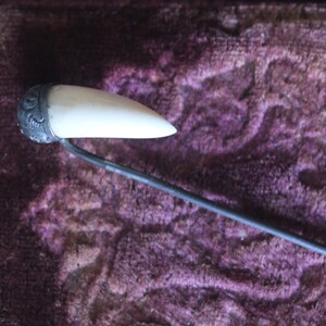 May include: A white bone hair pin with a silver decorative top. The pin is on a purple velvet surface.