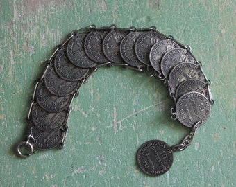 May include: A vintage silver bracelet made of connected coins. Each coin is stamped with the text "REPUBBLICA DI S. MARINO" and "10 CENTESIMI" along with the year "1936". The bracelet is displayed on a distressed green surface.
