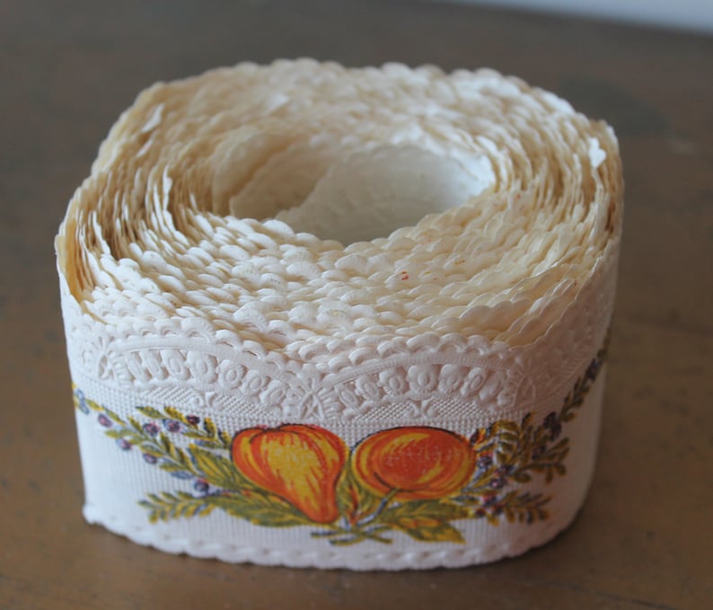 Puede incluir: Un rollo de encaje de papel blanco con un borde festoneado y un dise&ntilde;o impreso de peras naranjas y hojas verdes.