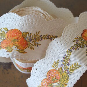 Puede incluir: Borde de encaje blanco con un borde festoneado y un patr&oacute;n repetido de fruta naranja y hojas verdes. El borde est&aacute; enrollado y listo para ser utilizado para manualidades o decoraci&oacute;n.