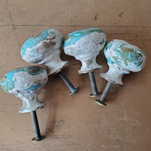 May include: Four vintage cabinet knobs with a distressed white and turquoise paint finish. The knobs have a round shape and a metal stem.