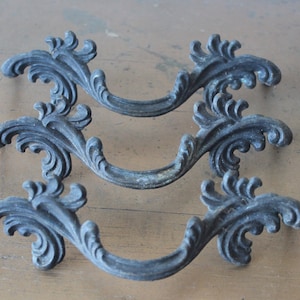 May include: Three antique-style drawer pulls with a decorative, ornate design. The pulls are made of metal and have a dark, aged finish.