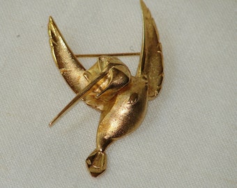 Puede incluir: Un broche de colibrí dorado con un diseño detallado. El colibrí está en vuelo con las alas extendidas. El broche tiene un pasador en la parte posterior para sujetarlo a la ropa.