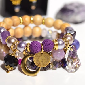Può includere: Un bracciale a più strati con perline in legno marrone chiaro, perline in pietra lavica viola, sfere color lavanda lisce e cristalli neri sfaccettati. Include ciondoli in metallo dorato a forma di mezzaluna e di sole con un volto.