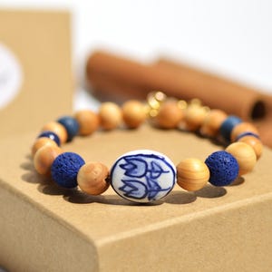 以下が含まれることがあります： 木製のビーズ、青い溶岩ビーズ、青い花の模様のセラミックビーズを特徴とするビーズブレスレット。 ブレスレットは茶色の箱に展示されています。