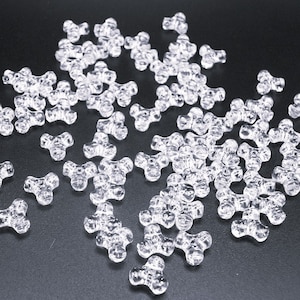 May include: A large quantity of clear plastic beads in the shape of a three-pointed star. The beads are scattered on a black surface.