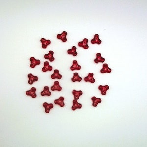 May include: A group of red, three-pointed plastic beads. The beads are scattered on a white surface.