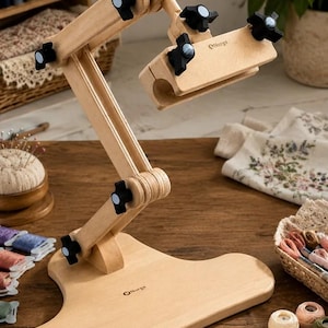 Puede incluir: Un soporte de madera clara para bastidores de bordado con brazo articulado ajustable y base plana. El soporte cuenta con perillas de plástico negro para ajustar las articulaciones y el logotipo de la marca Nurge impreso en la base y el soporte.