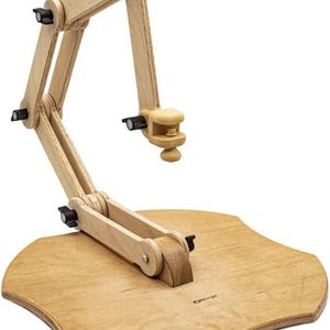 May include: A wooden embroidery stand with a natural finish. The stand features an adjustable arm with black knobs and a clamp, mounted on a wooden base. The base has a unique, curved shape. The stand is designed for holding embroidery hoops or frames.