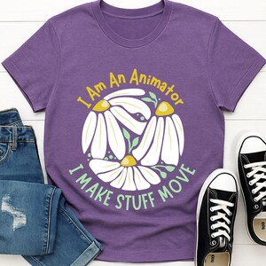 以下が含まれることがあります： 白いヒナギクと緑の葉のデザインで「I Am An Animator I Make Stuff Move」というテキストが入った紫色のTシャツ。 このシャツは、青いジーンズと黒いキャンバススニーカーと組み合わせています。