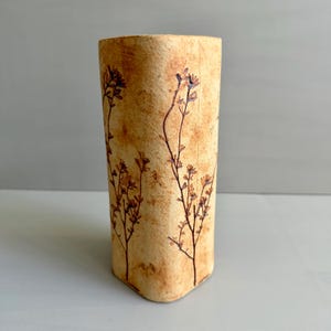 Peut inclure: Un vase rectangulaire et haut avec une surface beige texturée. De délicats motifs floraux bruns sont imprimés sur le vase. Le vase a une forme légèrement conique et convient pour exposer des fleurs ou comme objet décoratif.