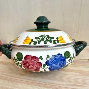 May include: White enamel cooking pot with a green lid and handles. The pot is decorated with hand-painted flowers in yellow, red, and blue. The rim is silver.