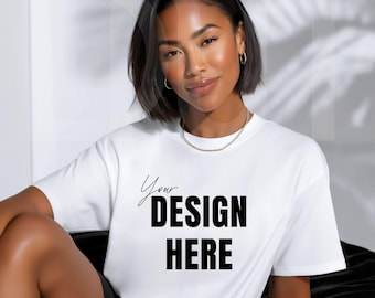 May include: A white t-shirt with the text "Your DESIGN HERE" in black. The model is wearing a gold chain necklace and hoop earrings. The model is sitting down.