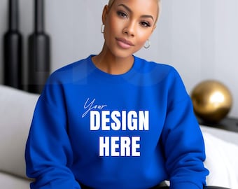 May include: A royal blue sweatshirt with the text "Your DESIGN HERE" in white. The sweatshirt is a solid color and has a crew neck. The model is wearing black leather pants. The background includes decorative black bottles and a gold sphere.