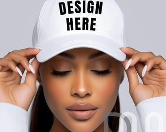 May include: A white baseball cap with the text "DESIGN HERE" in bold black letters. The cap is being held by a person with their eyes closed. The background is a light gray.